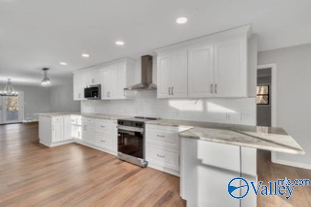 kitchen with a peninsula, light countertops, white cabinets, appliances with stainless steel finishes, and wall chimney exhaust hood