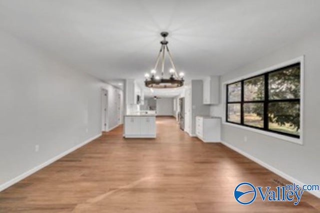 unfurnished dining area with a notable chandelier, baseboards, and light wood finished floors