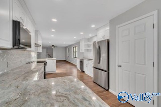 kitchen with tasteful backsplash, light stone counters, appliances with stainless steel finishes, a peninsula, and white cabinetry