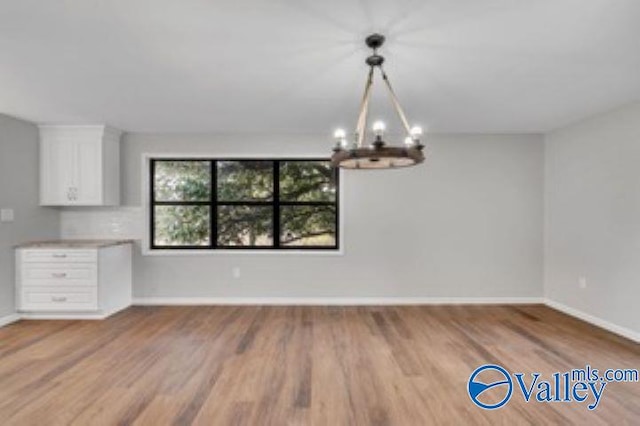 unfurnished dining area featuring a chandelier, baseboards, and wood finished floors