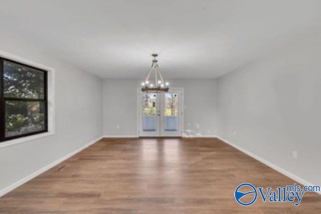 unfurnished dining area with baseboards, a notable chandelier, and wood finished floors