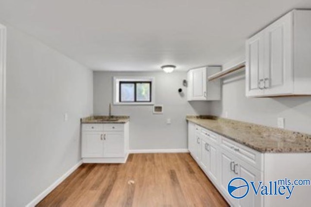 kitchen featuring baseboards, light stone counters, white cabinetry, and light wood-style floors