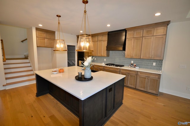 kitchen with stainless steel gas cooktop, a spacious island, light wood-type flooring, and custom exhaust hood