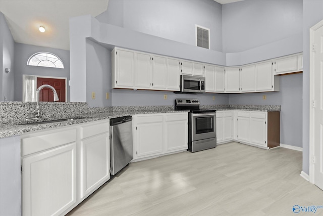 kitchen with white cabinetry, a high ceiling, light stone counters, light hardwood / wood-style floors, and appliances with stainless steel finishes