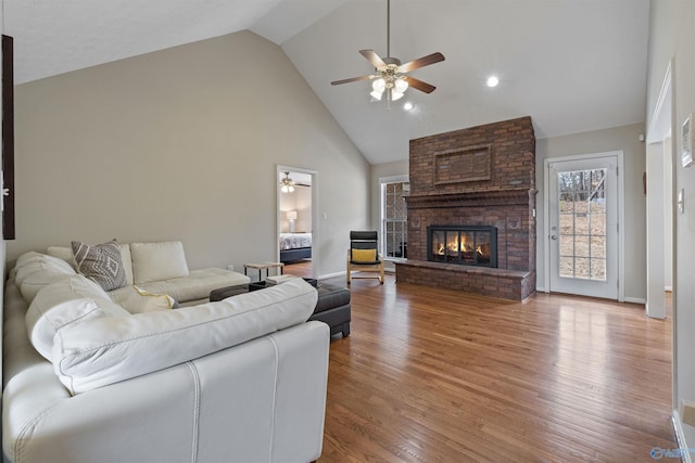 living room with a brick fireplace, hardwood / wood-style floors, high vaulted ceiling, and ceiling fan