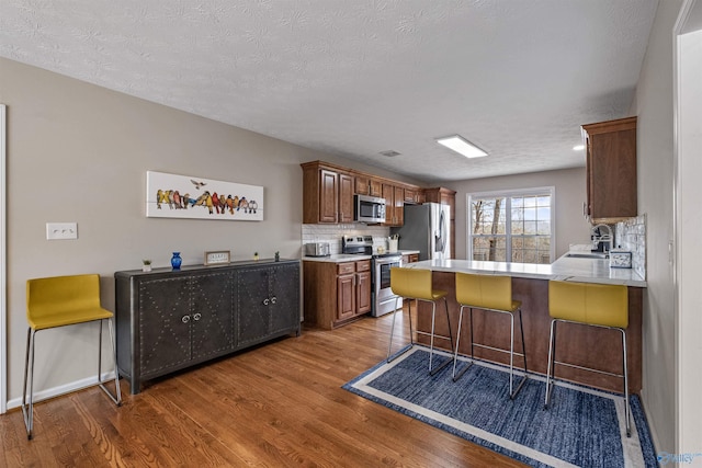 kitchen with a breakfast bar, decorative backsplash, kitchen peninsula, stainless steel appliances, and dark wood-type flooring