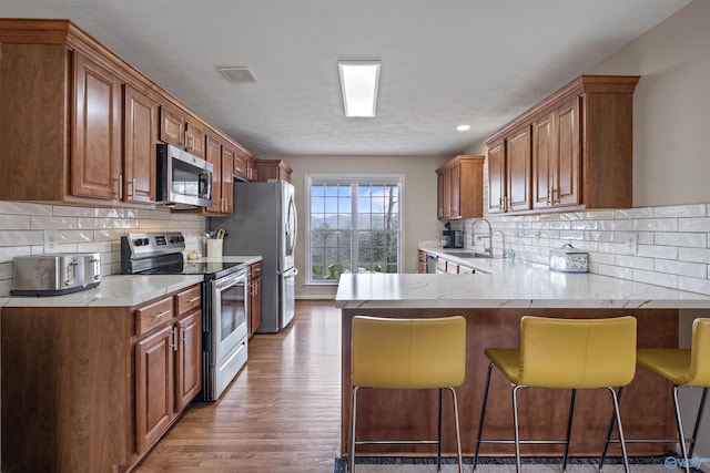 kitchen with appliances with stainless steel finishes, sink, a kitchen breakfast bar, kitchen peninsula, and dark wood-type flooring