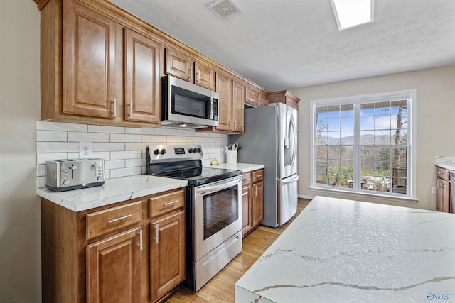 kitchen with stainless steel appliances, light stone countertops, light hardwood / wood-style flooring, and decorative backsplash