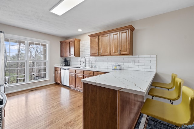 kitchen with sink, a breakfast bar, decorative backsplash, stainless steel dishwasher, and light wood-type flooring