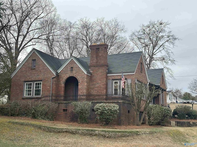 english style home featuring a chimney, a front lawn, and brick siding