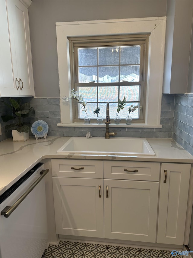 kitchen with tasteful backsplash, white cabinetry, a sink, light stone countertops, and dishwasher