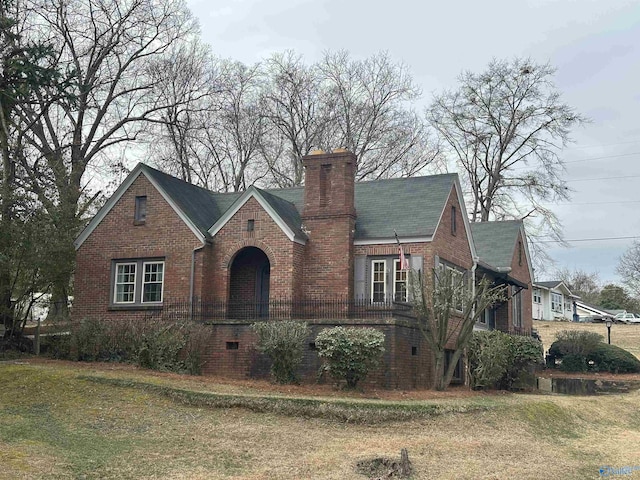 tudor house with a chimney, a front lawn, and brick siding