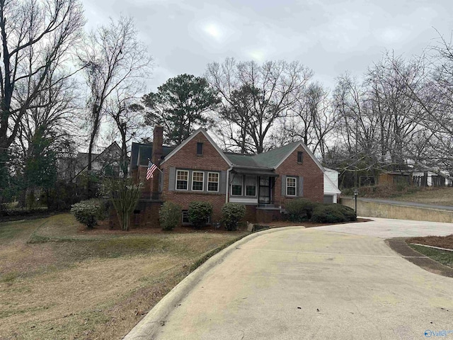 view of front of house featuring brick siding, a front lawn, and a chimney