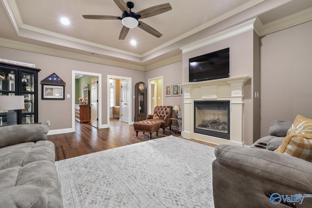 living room with ornamental molding, dark wood-type flooring, ceiling fan, and a tray ceiling