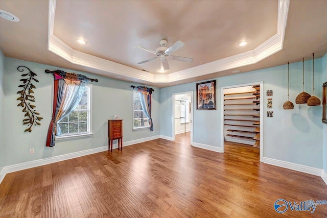 spare room featuring a raised ceiling, wood-type flooring, crown molding, and ceiling fan