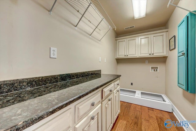 laundry area with light wood-type flooring, hookup for an electric dryer, hookup for a washing machine, and cabinets