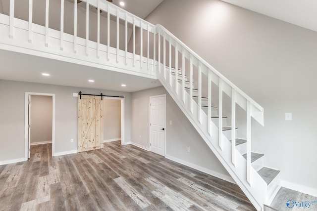 interior space with a barn door, stairs, baseboards, wood finished floors, and a towering ceiling
