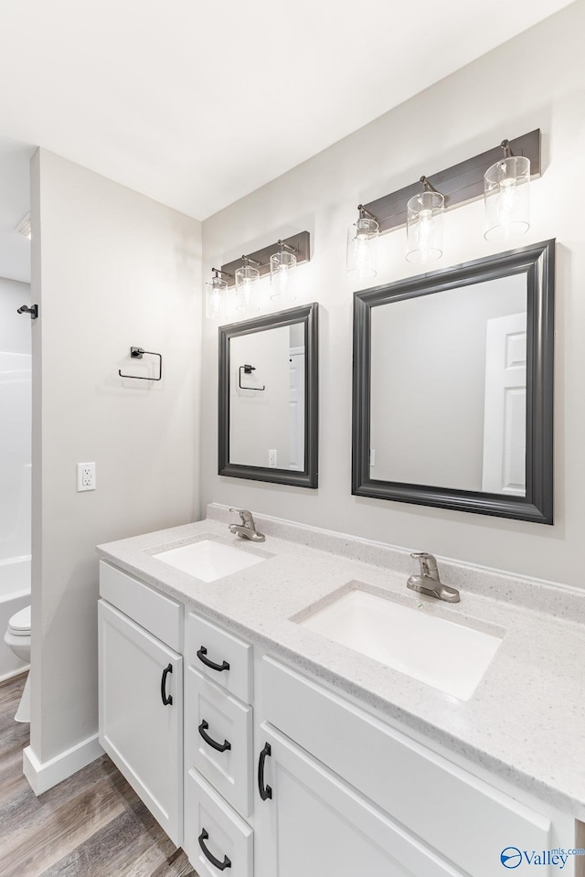 full bathroom with a sink, double vanity, toilet, and wood finished floors