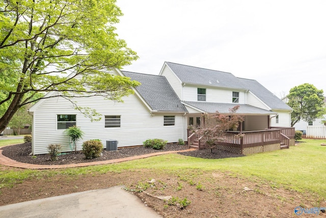 back of property with a lawn, roof with shingles, central AC, and a deck