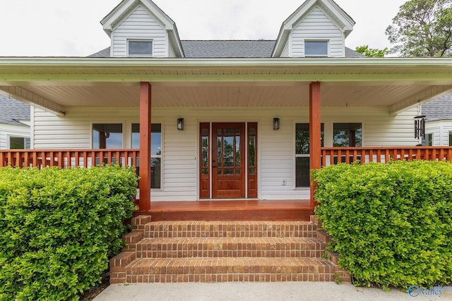doorway to property with covered porch and a shingled roof