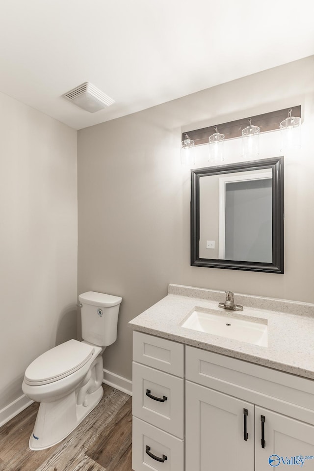 bathroom with vanity, visible vents, wood finished floors, toilet, and baseboards