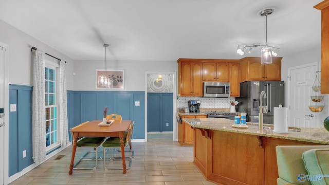 2317 Little Cove Rd, Owens Cross Roads, AL 35763 - kitchen with stainless steel appliances, light stone counters, a wainscoted wall, hanging light fixtures, and brown cabinetry