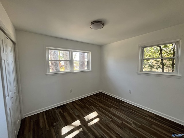 unfurnished bedroom with dark wood-type flooring, a closet, visible vents, and baseboards