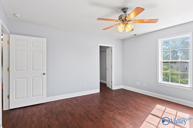 unfurnished bedroom featuring a spacious closet, ceiling fan, and dark hardwood / wood-style flooring