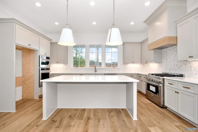 kitchen with stainless steel appliances, a kitchen island, hanging light fixtures, and light hardwood / wood-style floors