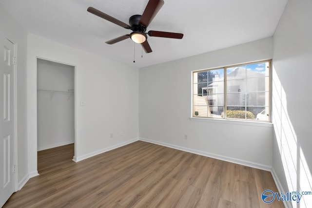 unfurnished bedroom with a closet, a spacious closet, ceiling fan, and hardwood / wood-style flooring