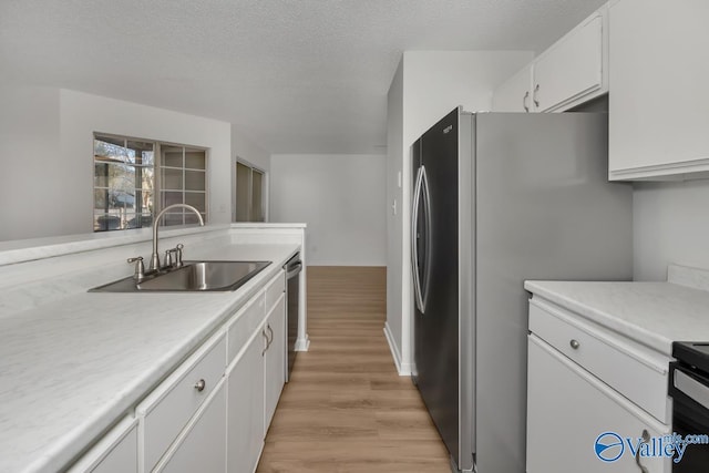 kitchen featuring white cabinetry, sink, light hardwood / wood-style floors, a textured ceiling, and appliances with stainless steel finishes