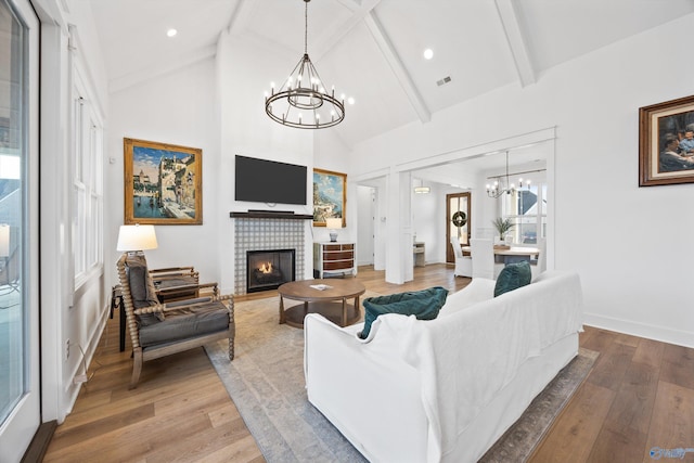 living room with a tiled fireplace, a notable chandelier, light hardwood / wood-style floors, and beam ceiling