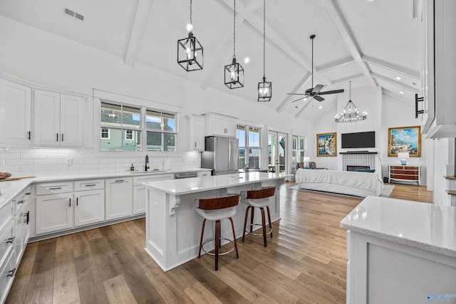 kitchen with sink, a tile fireplace, stainless steel refrigerator, white cabinetry, and a center island