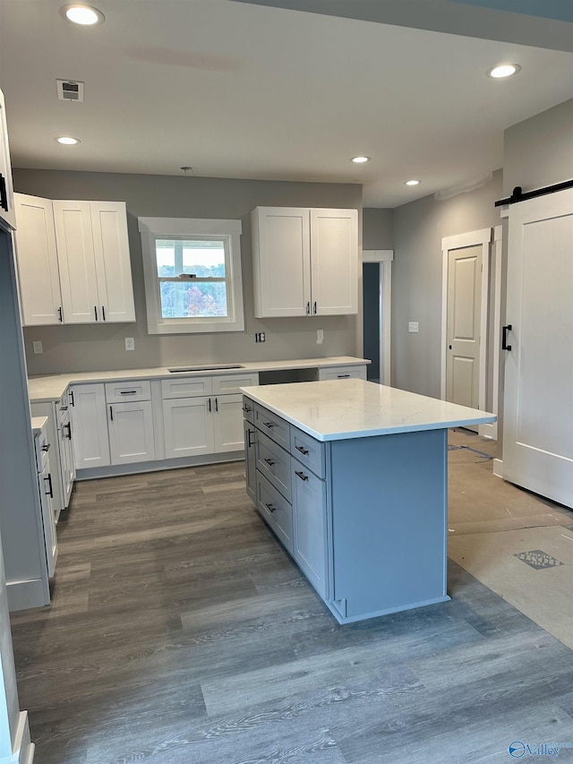 kitchen with white cabinets, a barn door, light hardwood / wood-style floors, a kitchen island, and light stone counters