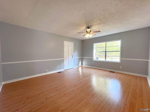 unfurnished room with ceiling fan, a textured ceiling, and light wood-type flooring