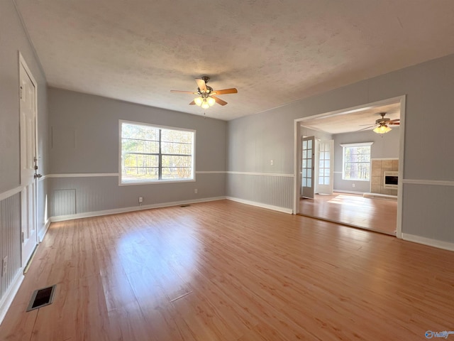 spare room featuring ceiling fan, a textured ceiling, light hardwood / wood-style flooring, and a tile fireplace