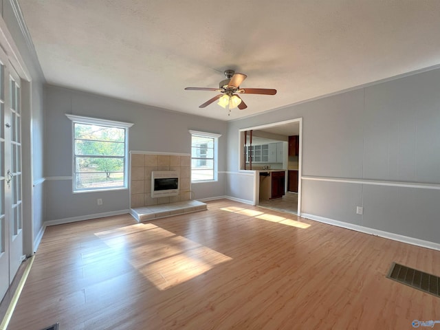 unfurnished living room with light hardwood / wood-style flooring, a tiled fireplace, heating unit, and ceiling fan