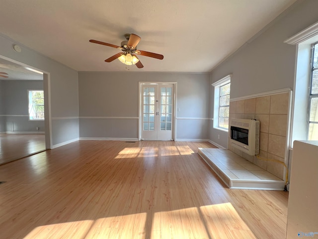 unfurnished living room featuring french doors, a tiled fireplace, heating unit, light wood-type flooring, and ceiling fan