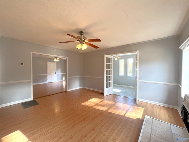 spare room with french doors, a stone fireplace, light hardwood / wood-style flooring, a textured ceiling, and ceiling fan