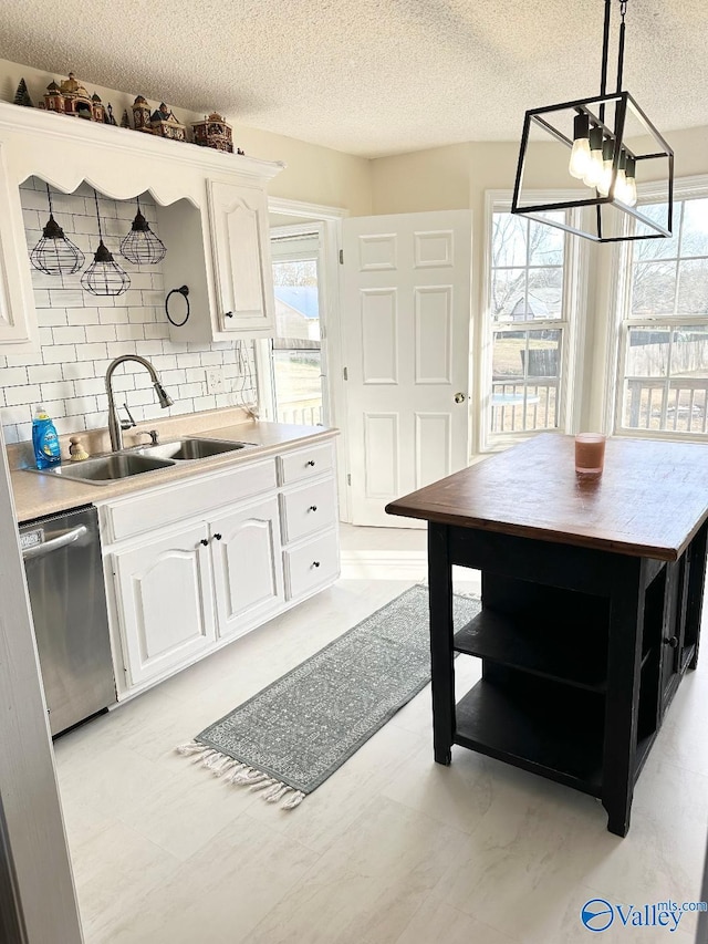 kitchen with pendant lighting, light countertops, stainless steel dishwasher, white cabinets, and a sink