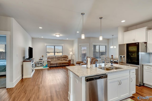 kitchen with stainless steel appliances, white cabinets, open floor plan, light wood finished floors, and a center island with sink