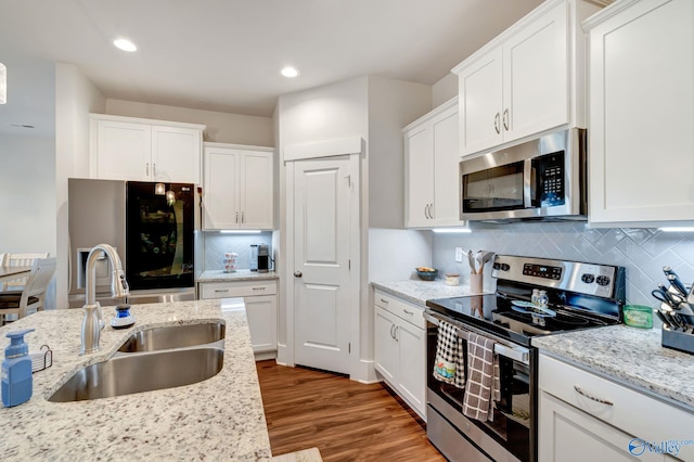 kitchen with wood finished floors, a sink, white cabinets, appliances with stainless steel finishes, and backsplash