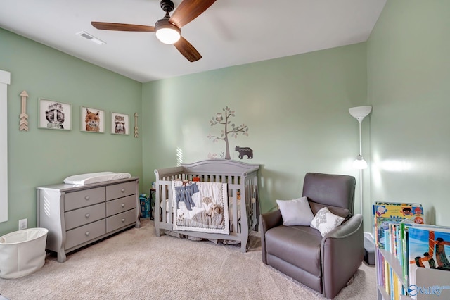 carpeted bedroom with a crib, visible vents, and a ceiling fan