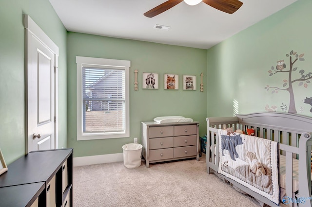 carpeted bedroom featuring a ceiling fan, a nursery area, visible vents, and baseboards