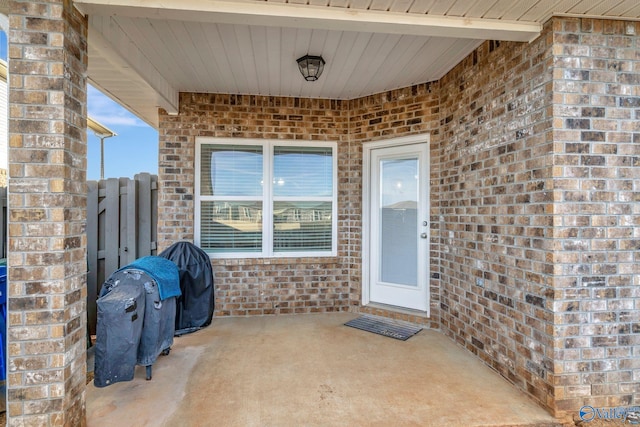 doorway to property featuring a patio, brick siding, and fence