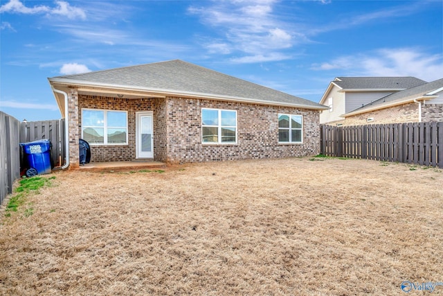 rear view of property with a fenced backyard, roof with shingles, and brick siding