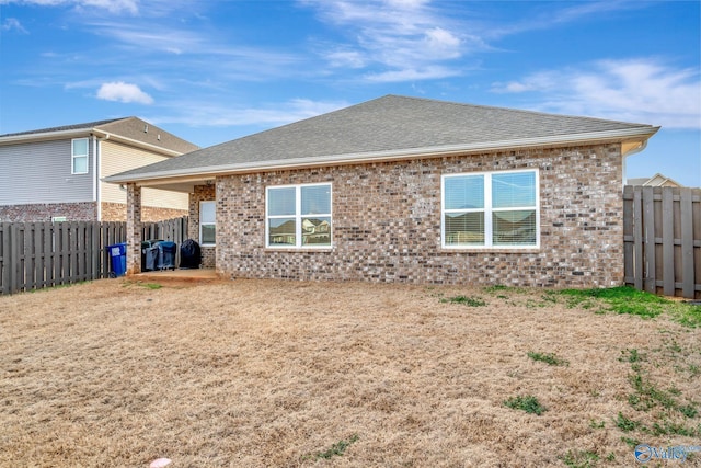 back of property featuring brick siding, a shingled roof, and a fenced backyard