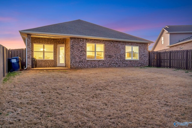 rear view of house with a shingled roof, brick siding, and a fenced backyard