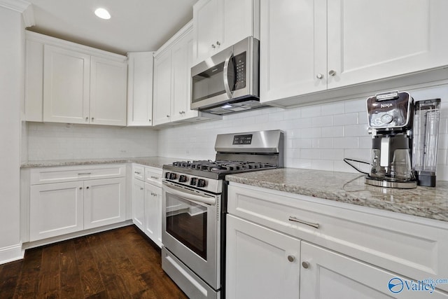 kitchen with white cabinets, appliances with stainless steel finishes, dark hardwood / wood-style flooring, backsplash, and light stone counters