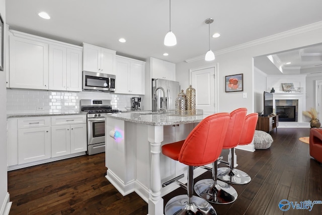 kitchen with white cabinets, stainless steel appliances, a kitchen island with sink, and decorative light fixtures